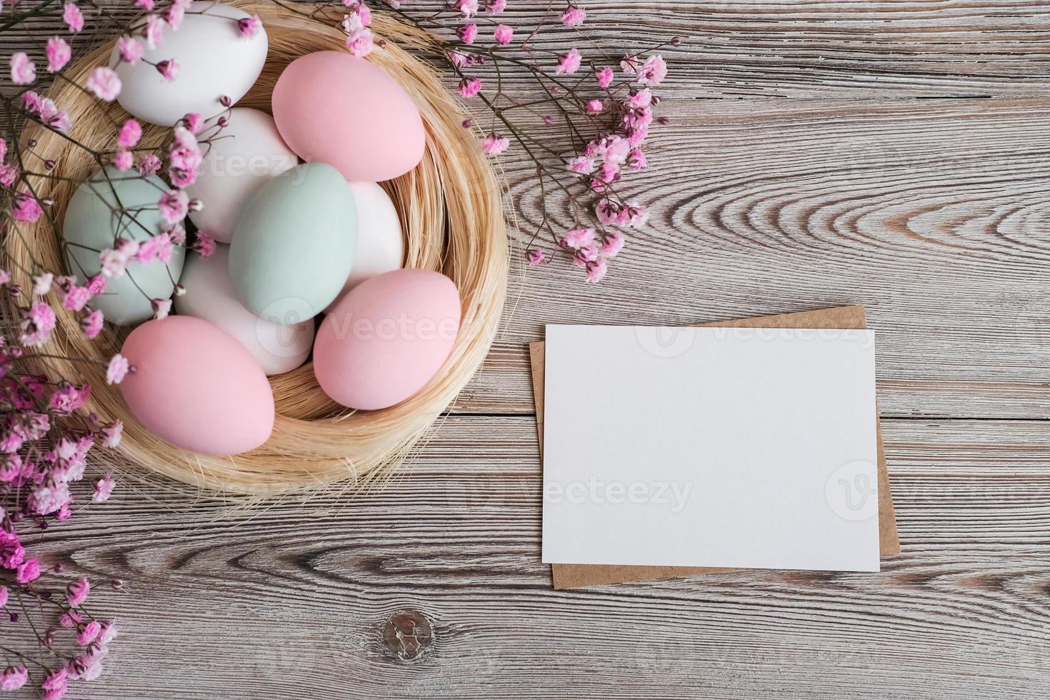 Pink flowers, a nest with eggs in soft pastel colors and blank white card for text on a wooden background. Mockup. Place for text. Easter card photo