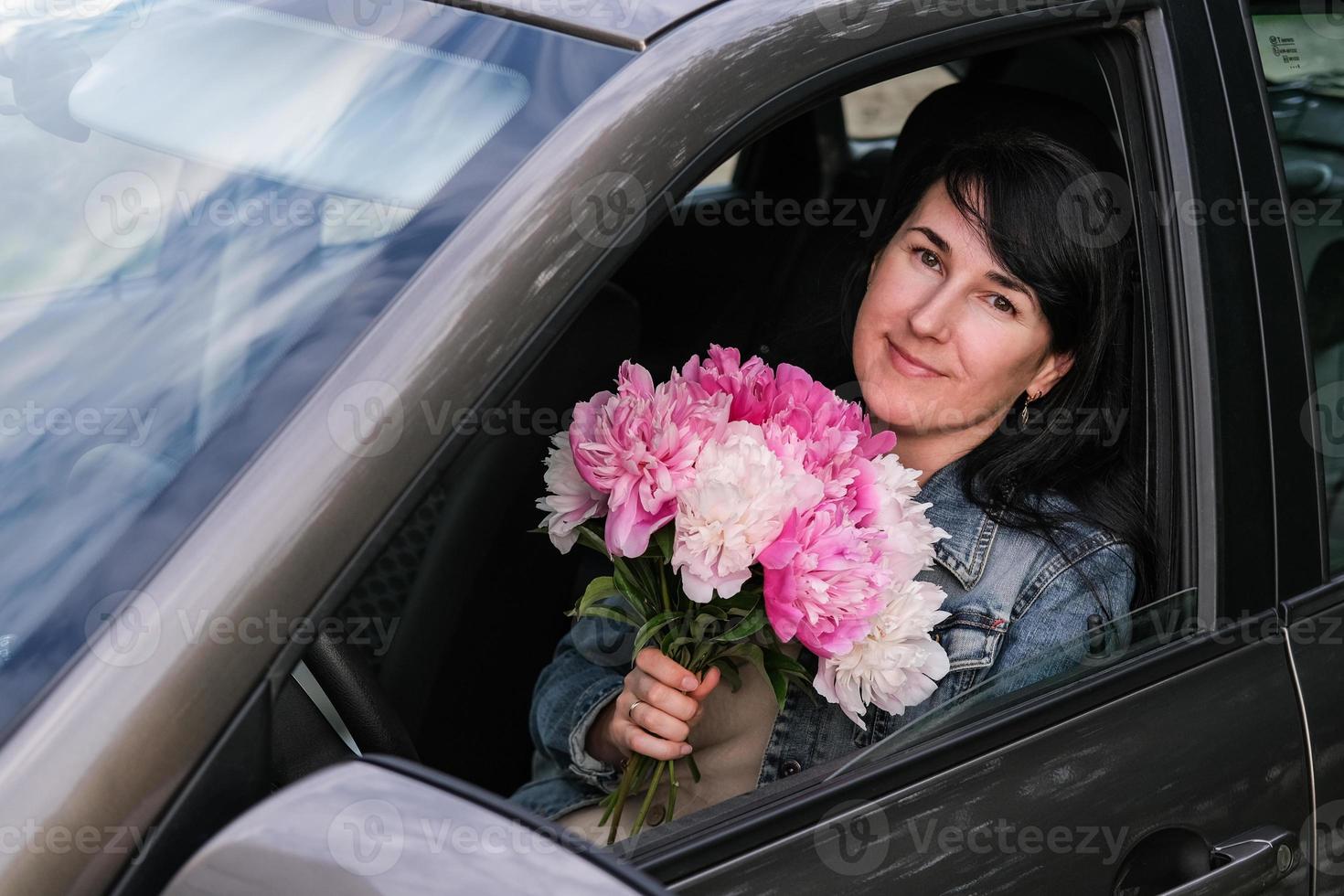 mujer sonriente joven con un ramo de flores sentado en el coche foto