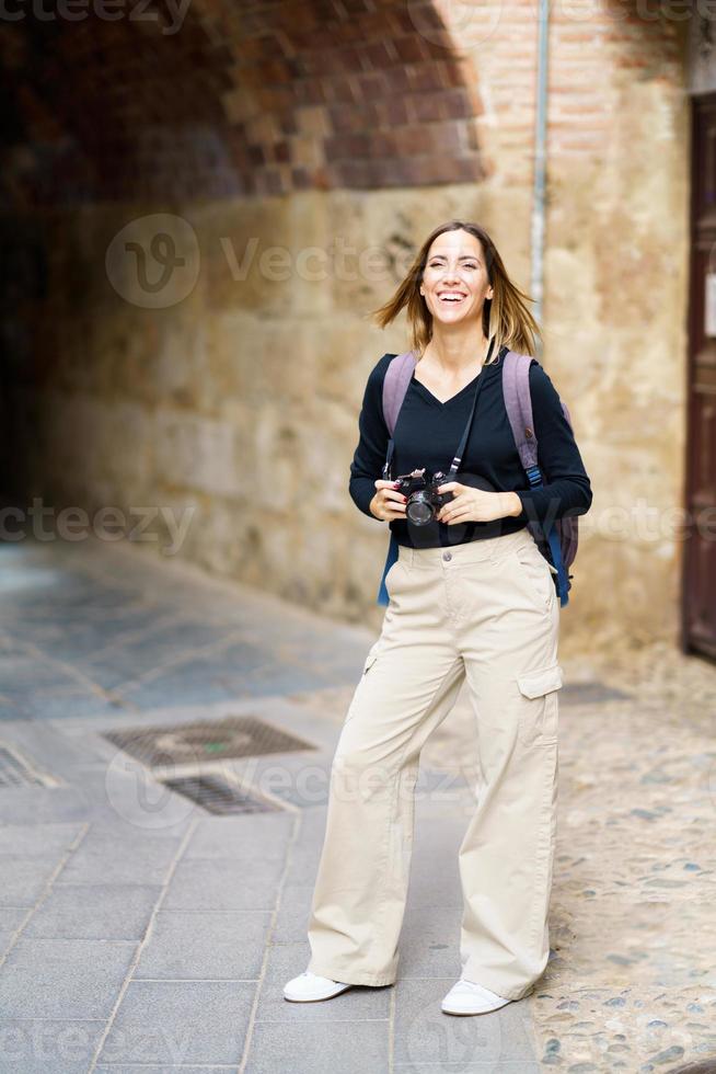 Positive female tourist with photo camera smiling near aged building