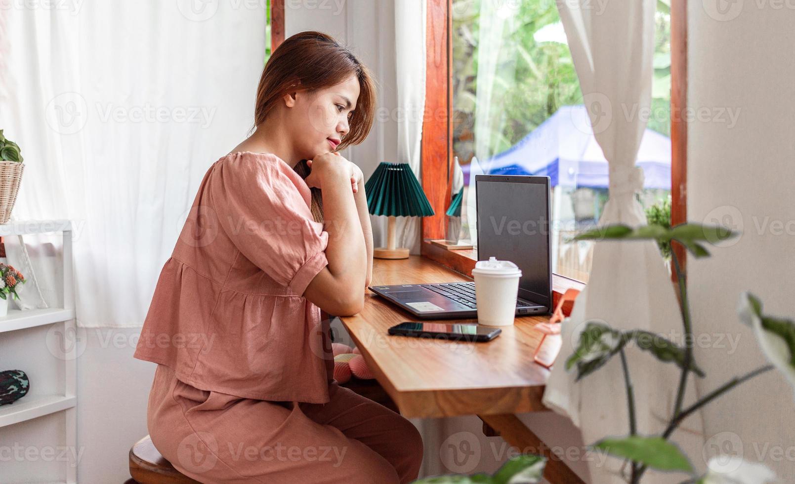 una mujer feliz en un café usando una computadora portátil. joven mujer blanca sentada en una cafetería ocupada trabajando en su computadora portátil. foto