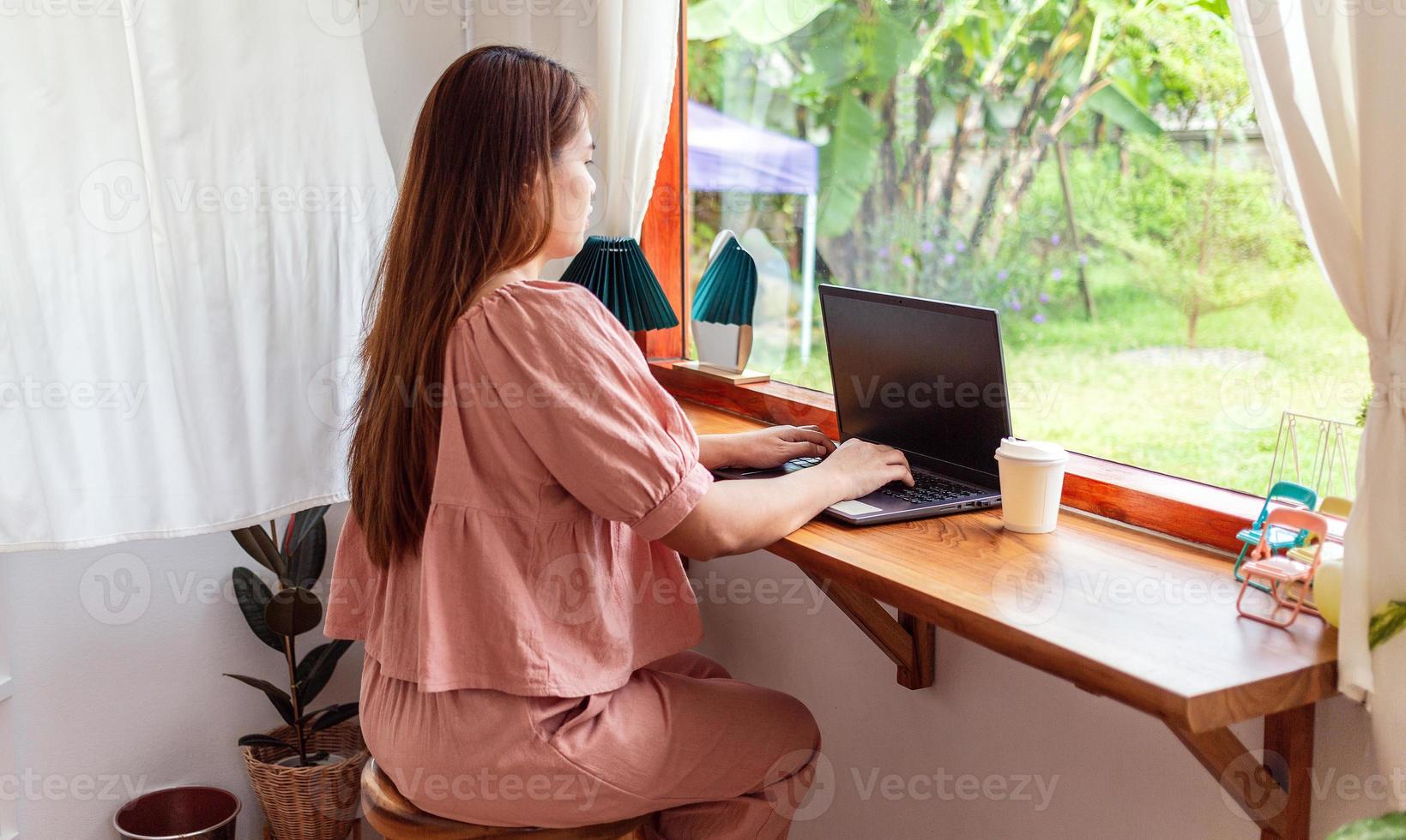 A happy woman in a pink shirt sits at a working laptop. Businesswoman busy working on laptop in cafe photo