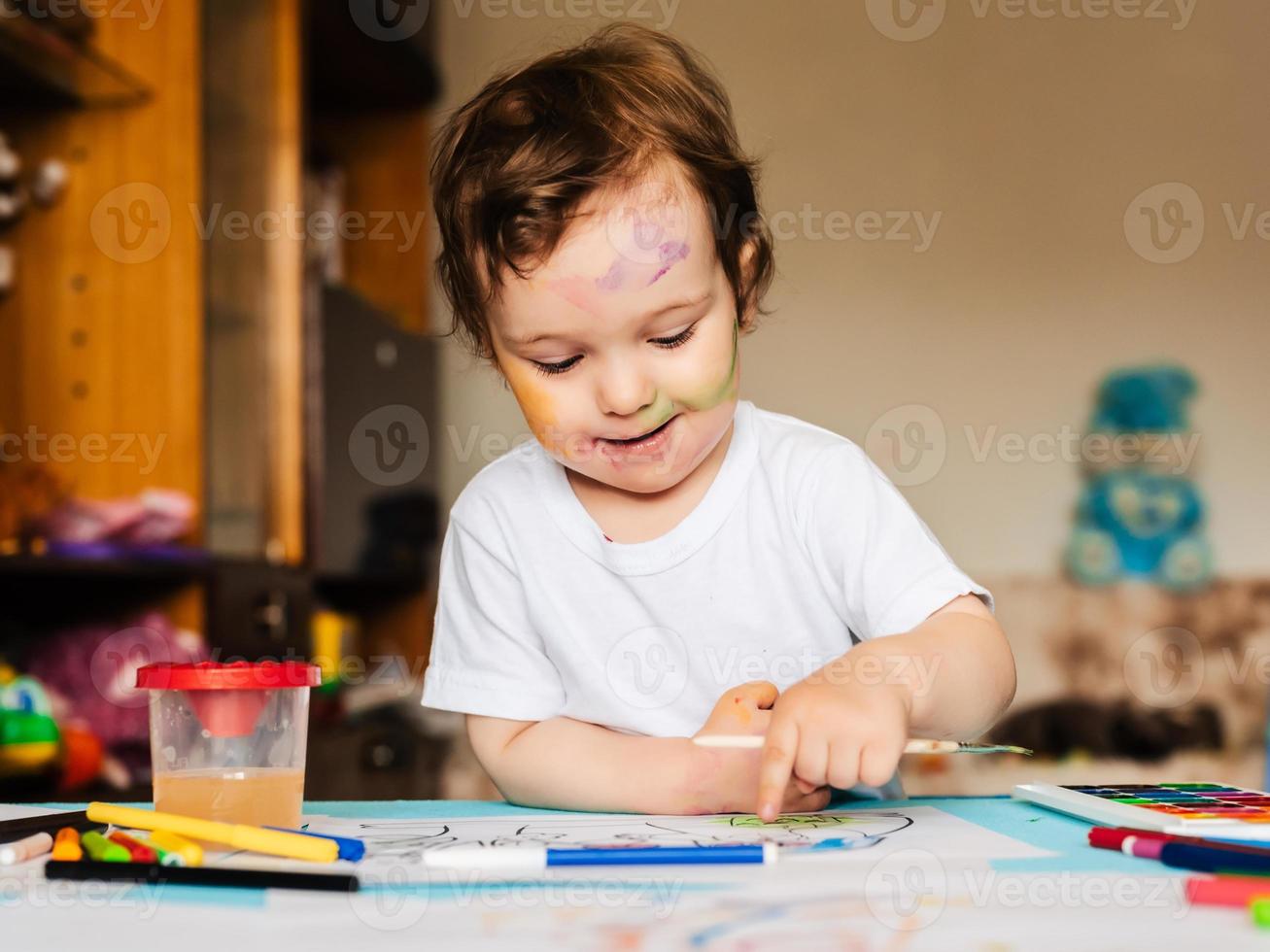 a small cute boy paints with brushes and colored paints on a sheet of paper photo