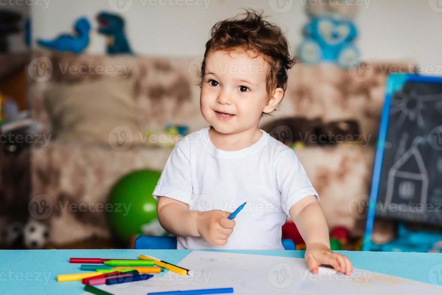 a small boy draws on sheets of paper lying on the table with colored pencils photo