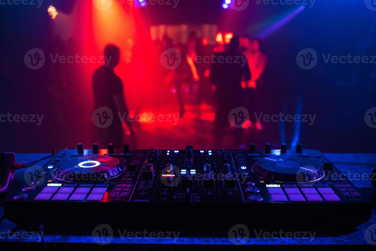 DJ console for mixing music with blurry people dancing at a nightclub party photo