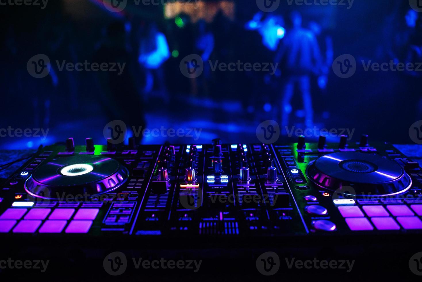 consola de dj para mezclar música con gente borrosa bailando en una fiesta de discoteca foto