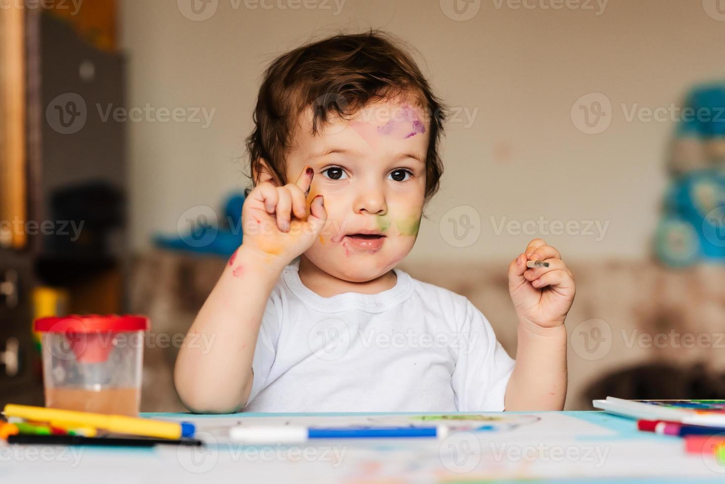 a small cute boy draws with brushes and colored paints on a sheet of paper photo