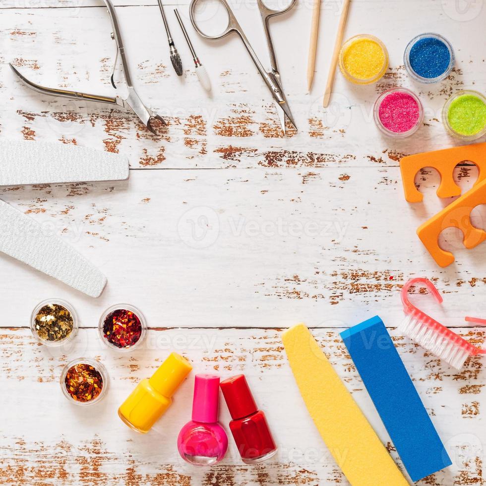 nail files, scissors, pliers, sequins and nail polishes on a white wooden background. with space for your text photo