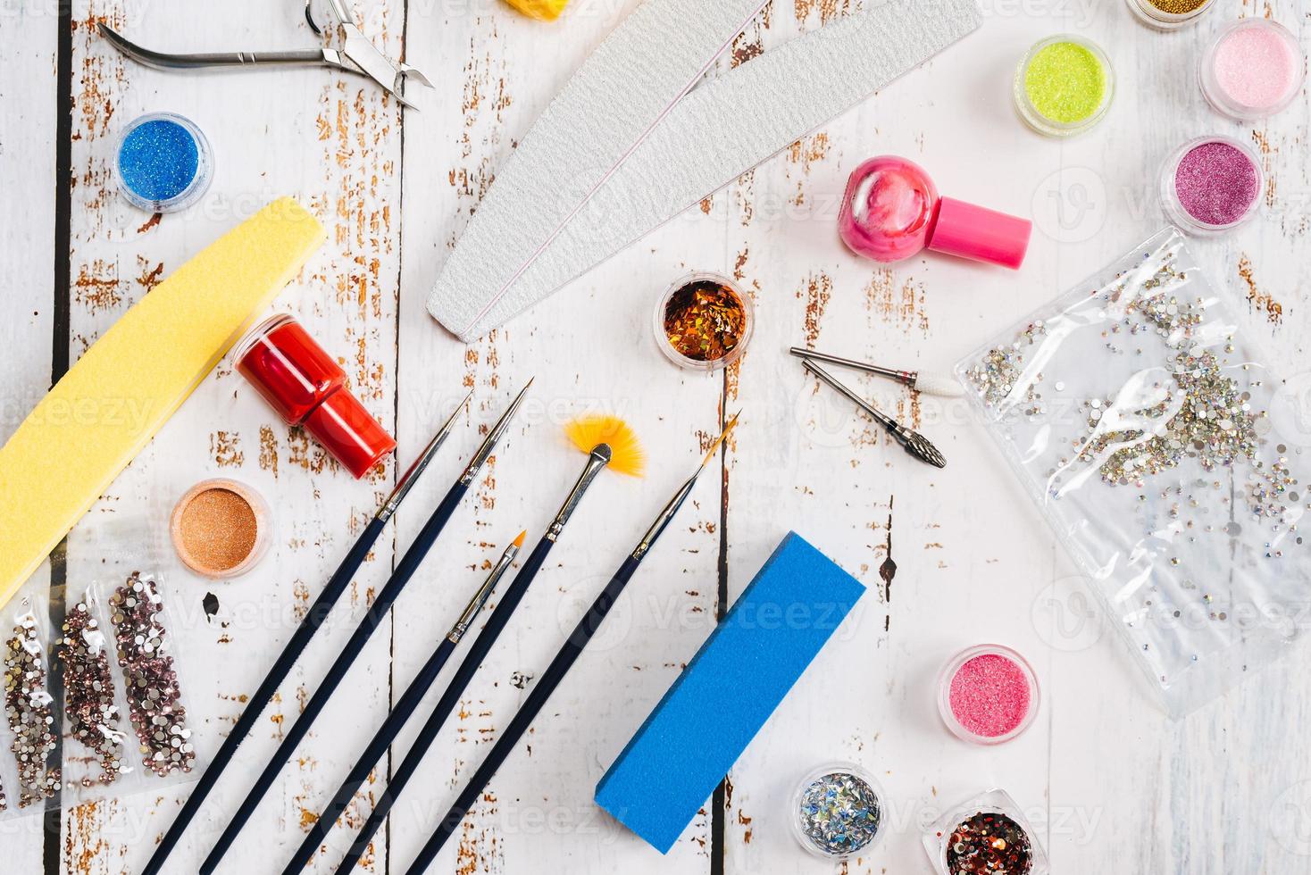 nail files, scissors, pliers, sequins and nail polishes on a white wooden background. photo