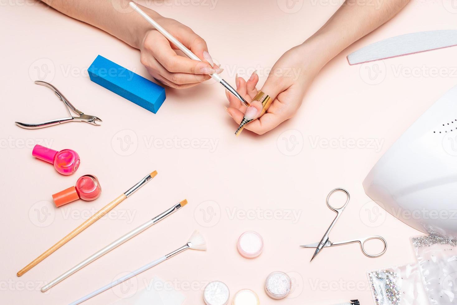 hands of a girl applying gel to her nails with a brush. the view from the top photo