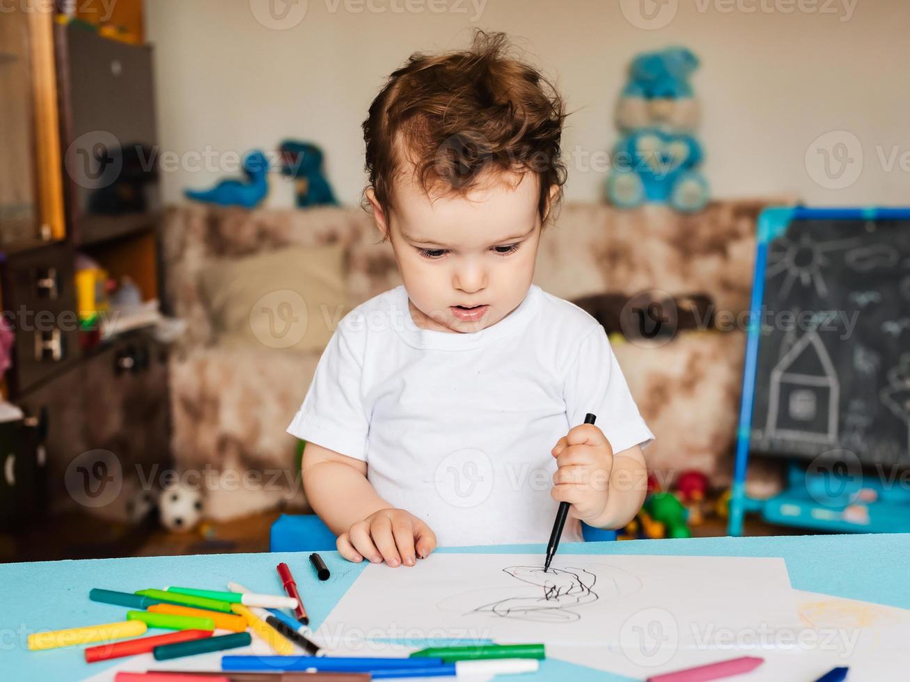 un niño pequeño se sienta en una silla y dibuja con lápices de colores foto