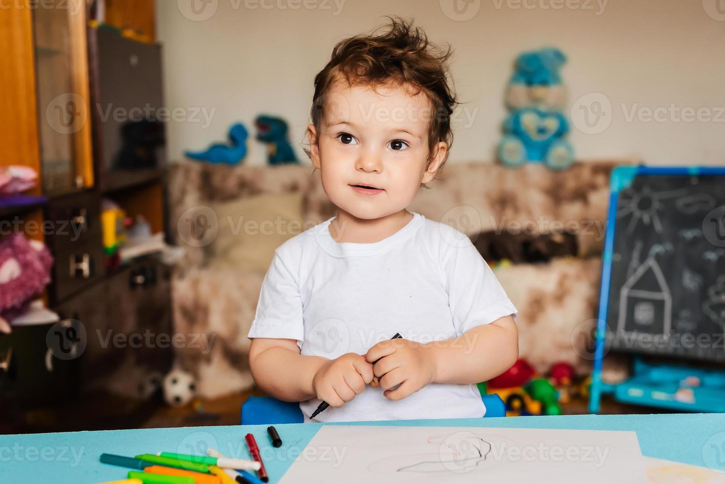 a small boy draws on sheets of paper lying on the table with colored pencils photo