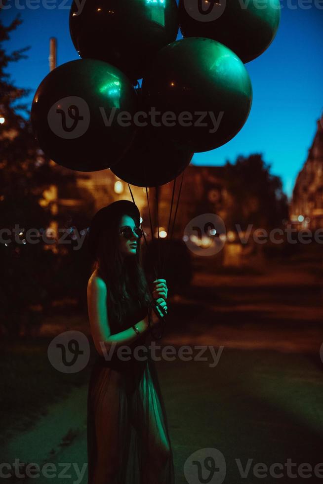 young girl in total black holds black balloons on the street photo