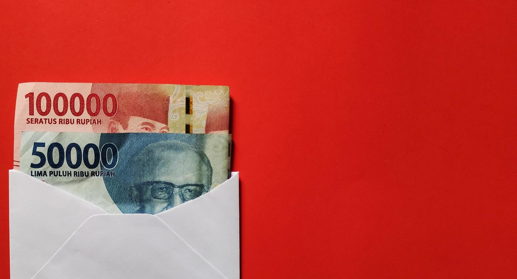 Indonesian rupiah nominal 50000 and 100000 rupiah in white envelope isolated on red background. photo