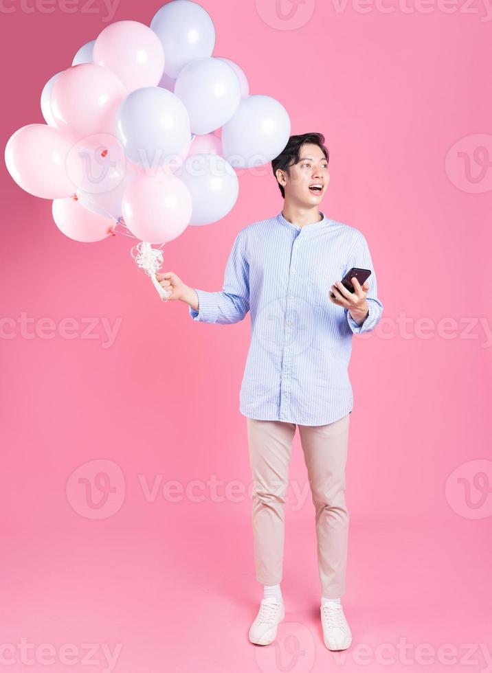 Young Asian man holding balloon on pink background photo