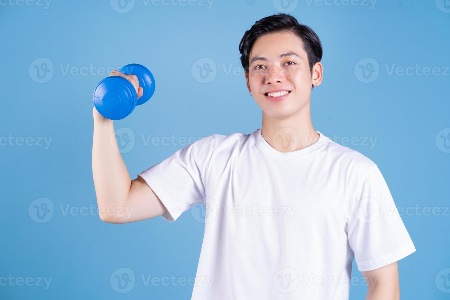 Young Asian man holding dumbbell on background photo