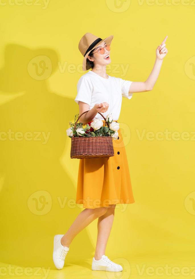 Full length photo of young Asian woman holding flower on yellow background