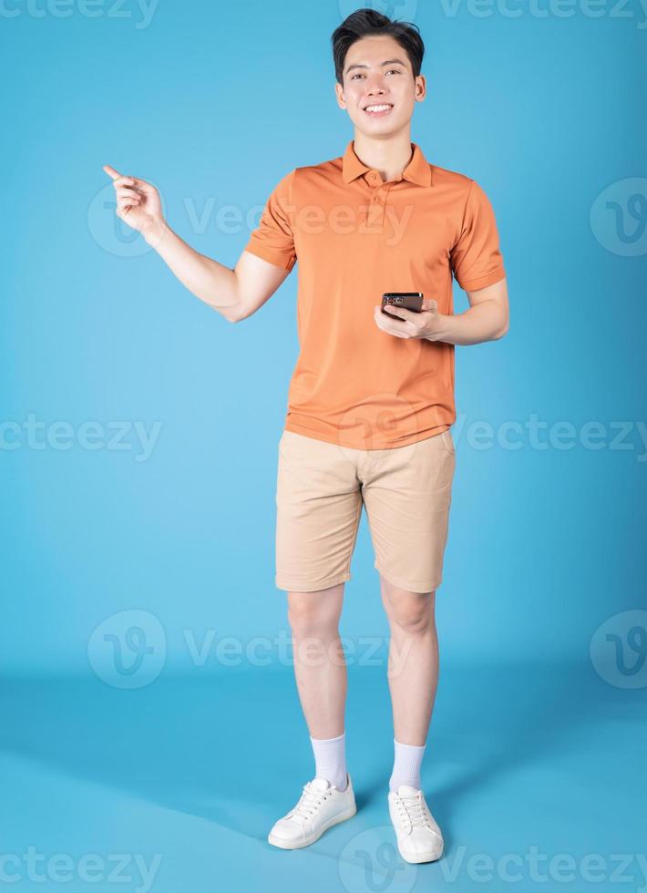 Image of young Asian man holding smartphone on blue background photo