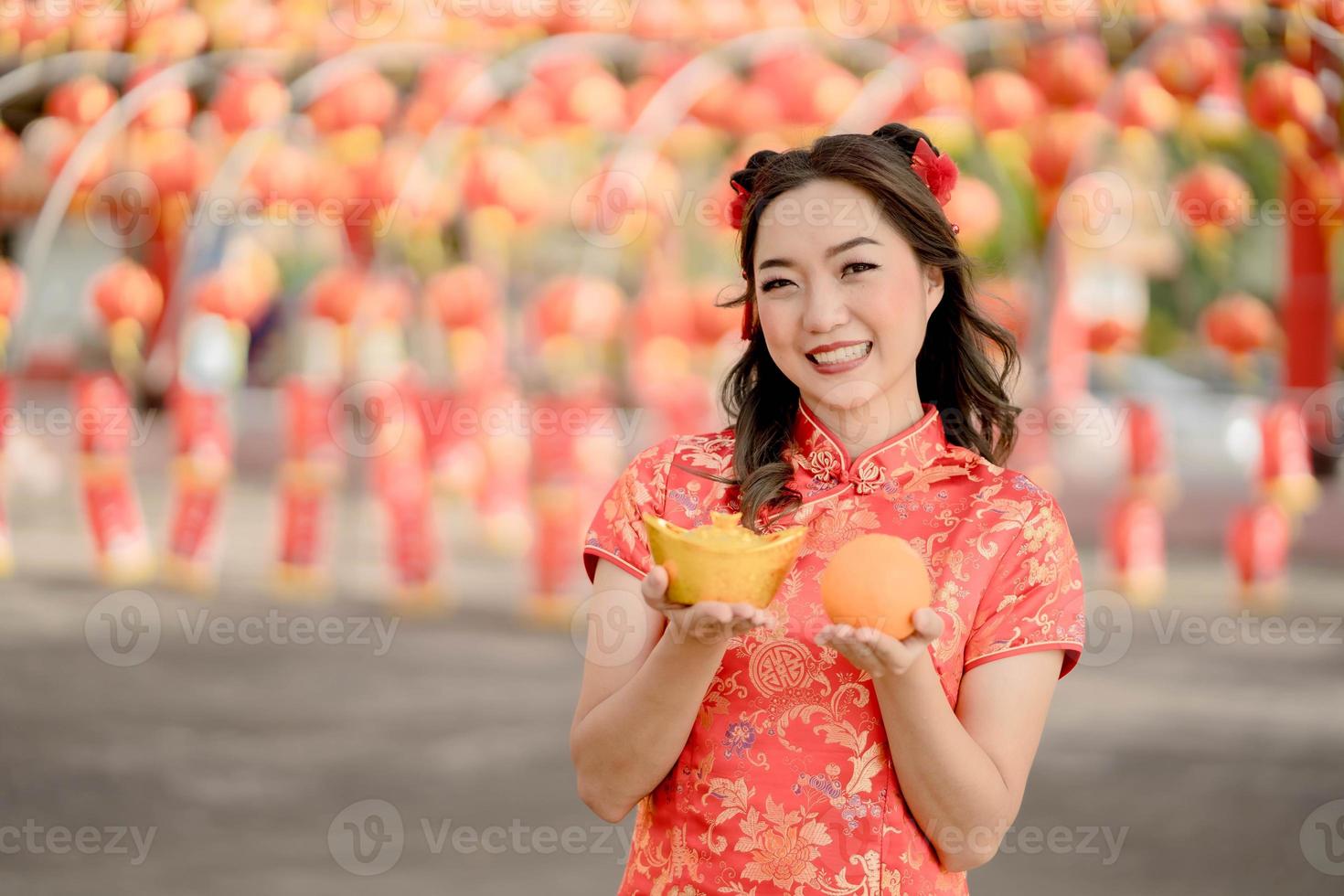 Happy Chinese new year. A young lady wearing traditional cheongsam qipao dress holding ancient gold money and orange fresh in Chinese Buddhist temple. Celebrate Chinese lunar new year. photo