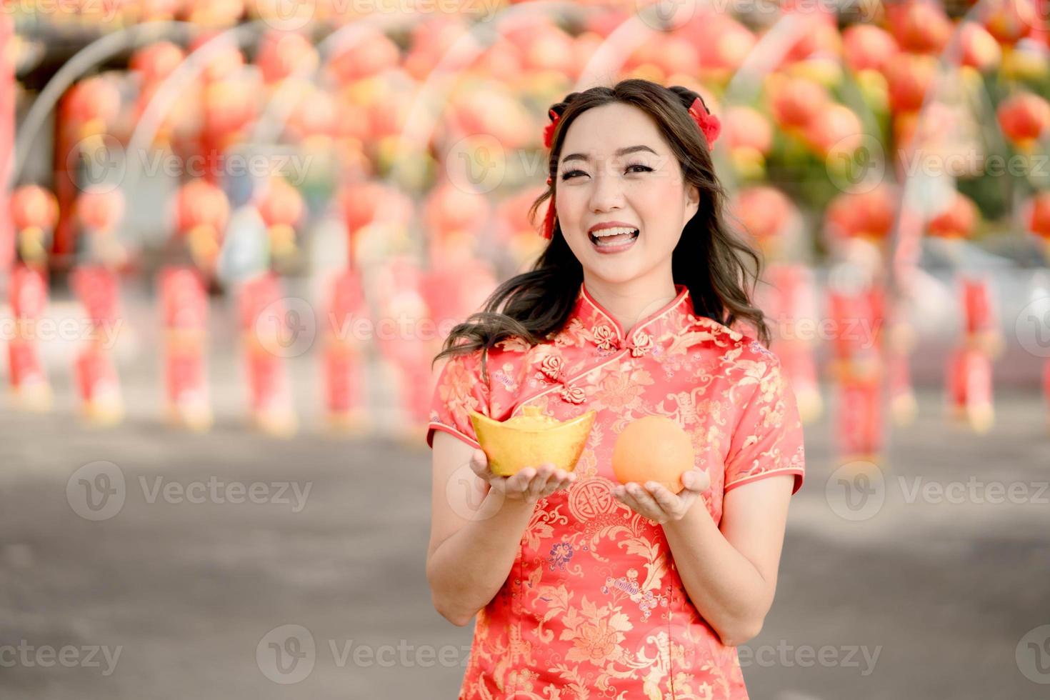 Happy Chinese new year. Beautiful  asian woman wearing traditional cheongsam qipao dress holding ancient gold money and orange fresh in Chinese Buddhist temple. Celebrate Chinese lunar new year. photo