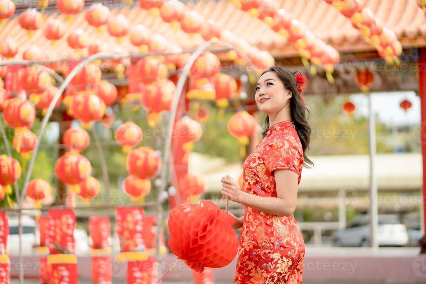 Happy Chinese new year. Beautiful Asian woman wearing traditional cheongsam qipao dress looking confident holding lantern while visiting the Chinese Buddhist temple photo