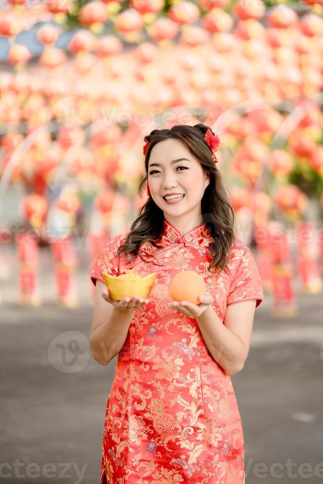 Vertical pictire. Happy Chinese new year. A young lady wearing traditional cheongsam qipao dress holding ancient gold money and orange fresh in Chinese Buddhist temple. photo