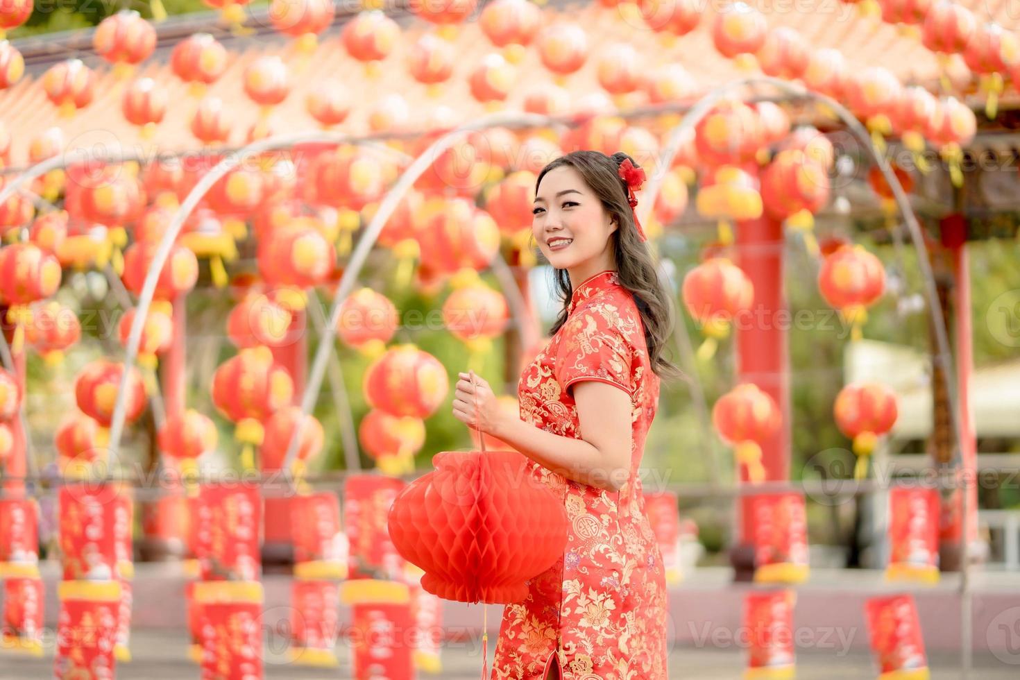 Happy Asian woman wearing traditional cheongsam qipao dress holding lantern while visiting the Chinese Buddhist temple. Chinese new year concept photo