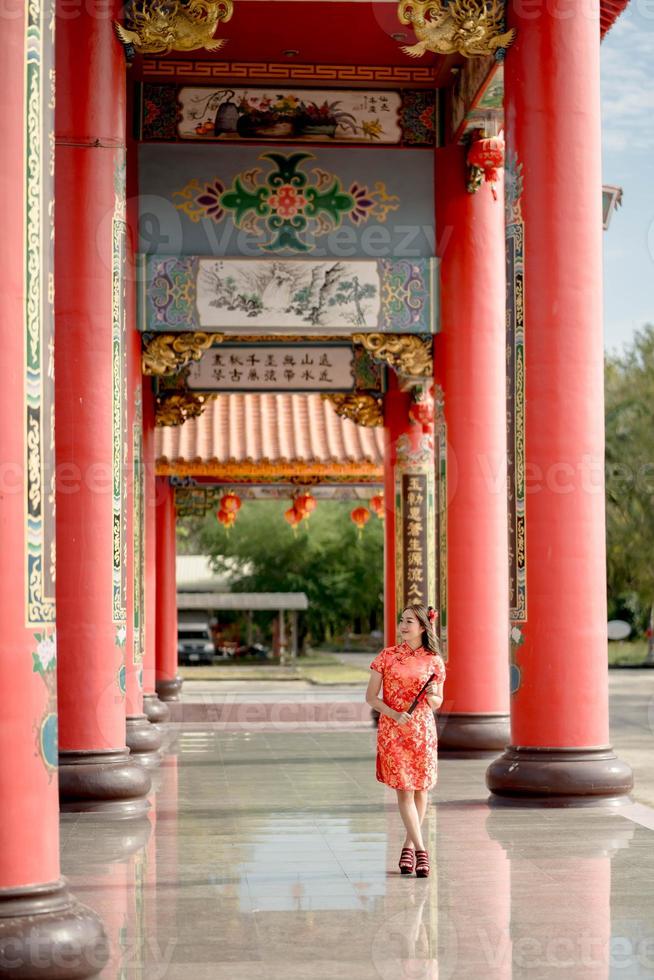 Vertical picture. A Asian woman wearing traditional cheongsam qipao dress holding fan and smile while visiting the Chinese Buddhist temple. Chinese new year concept photo