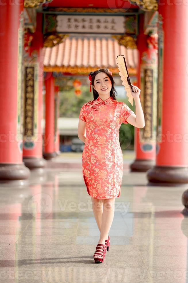 Vertical picture. Happy Chinese new year. A Asian woman wearing traditional cheongsam qipao dress holding fan and smile while visiting the Chinese Buddhist temple. Chinese new year concept photo