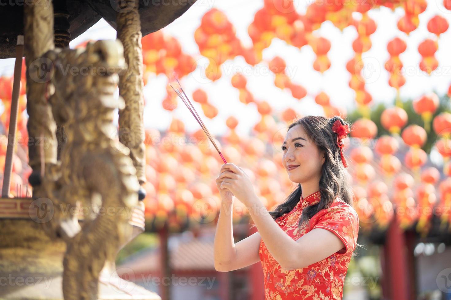 mujer asiática con vestido tradicional cheongsam qipao rezando con varitas de incienso por la mejor bendición y buena suerte en el templo budista chino. foto