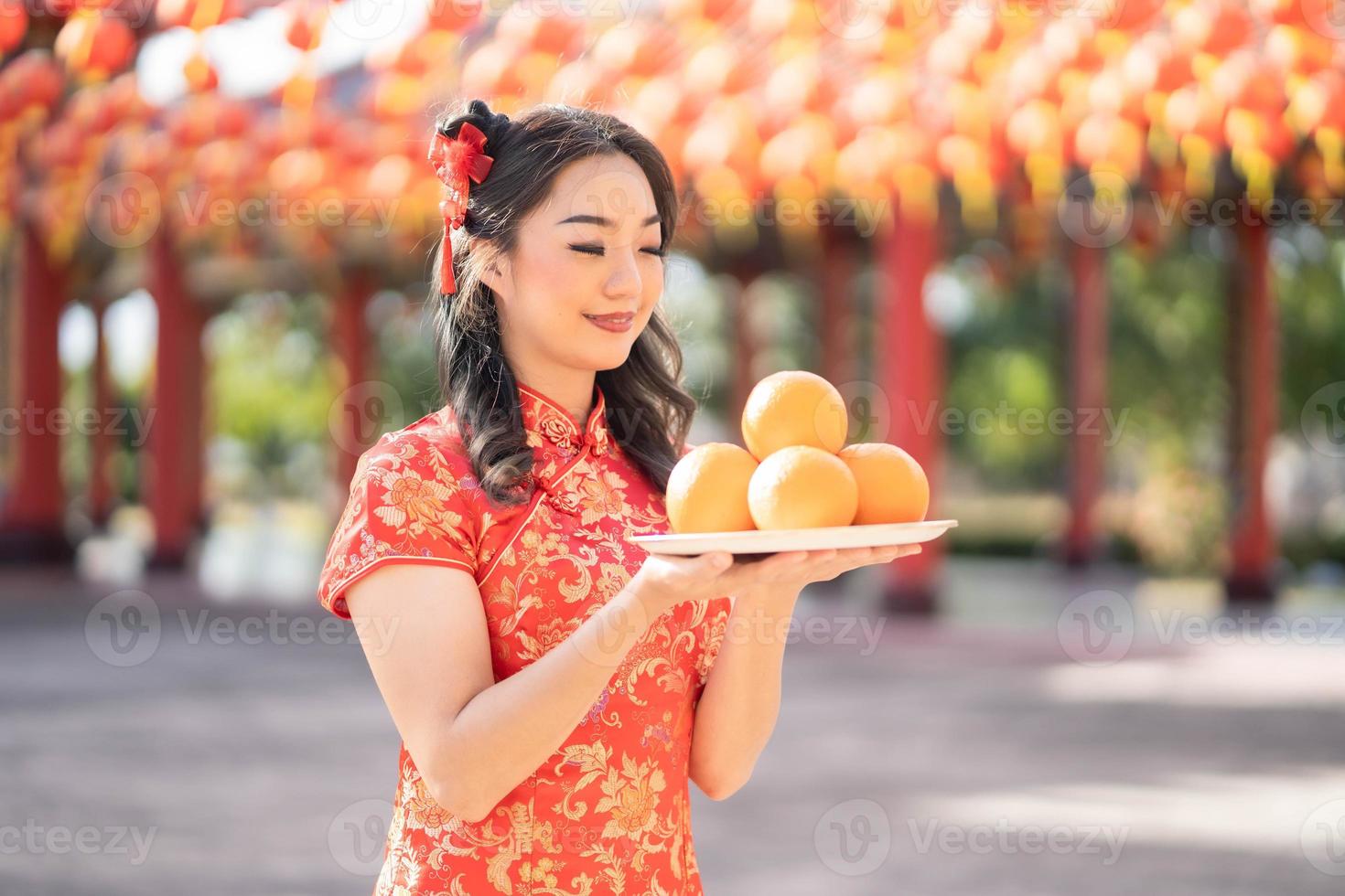 feliz Año Nuevo Chino. hermosa mujer asiática con vestido tradicional cheongsam qipao sosteniendo naranjas frescas en el templo budista chino. orar por el mejor deseo bendición y buena suerte foto