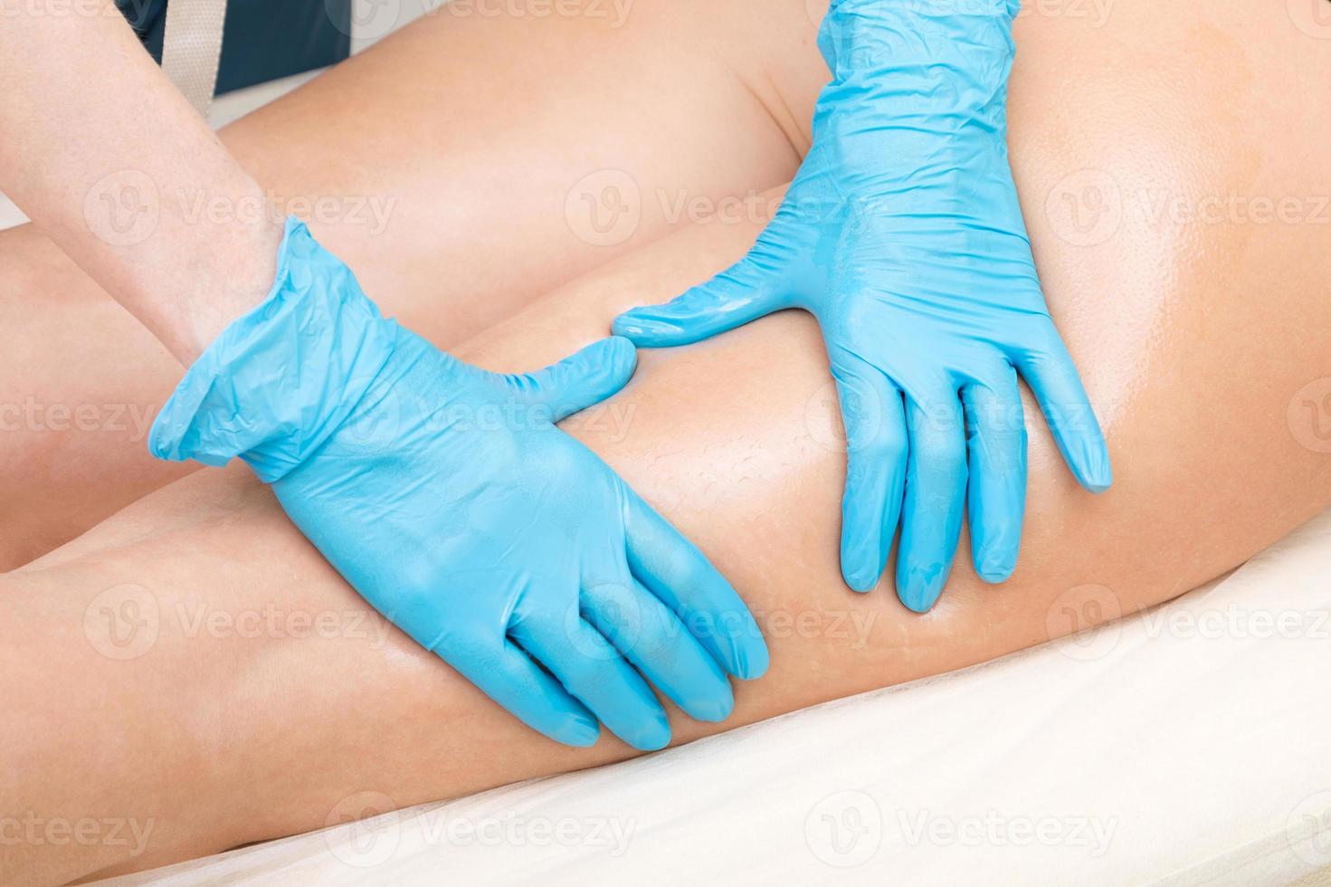 primer plano de una cosmetóloga manos en guantes azules haciendo masaje de nalgas foto