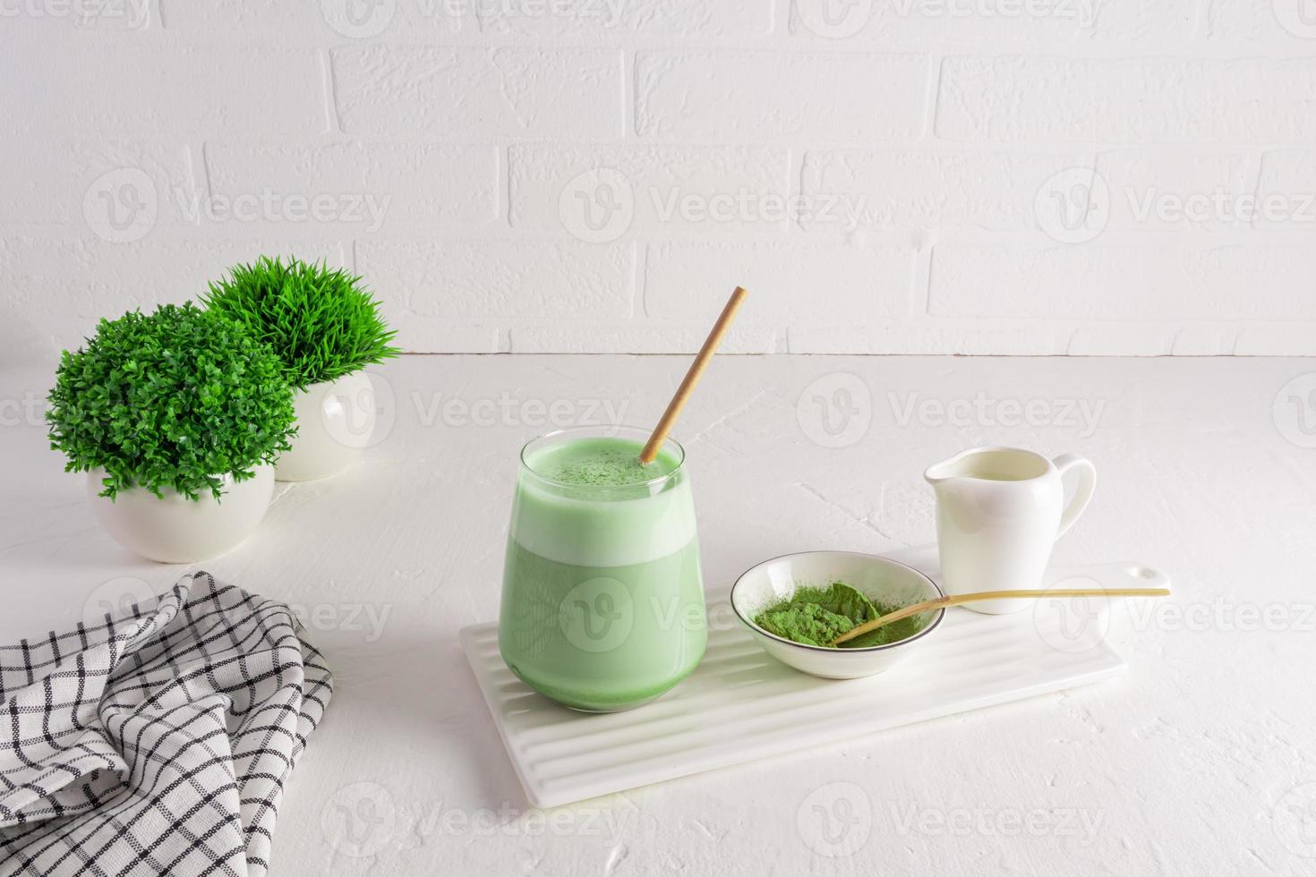 un gran vaso de té verde matcha latte y paja sobre una tabla de mármol blanco contra un fondo de paredes texturizadas y plantas en macetas. desintoxicación foto