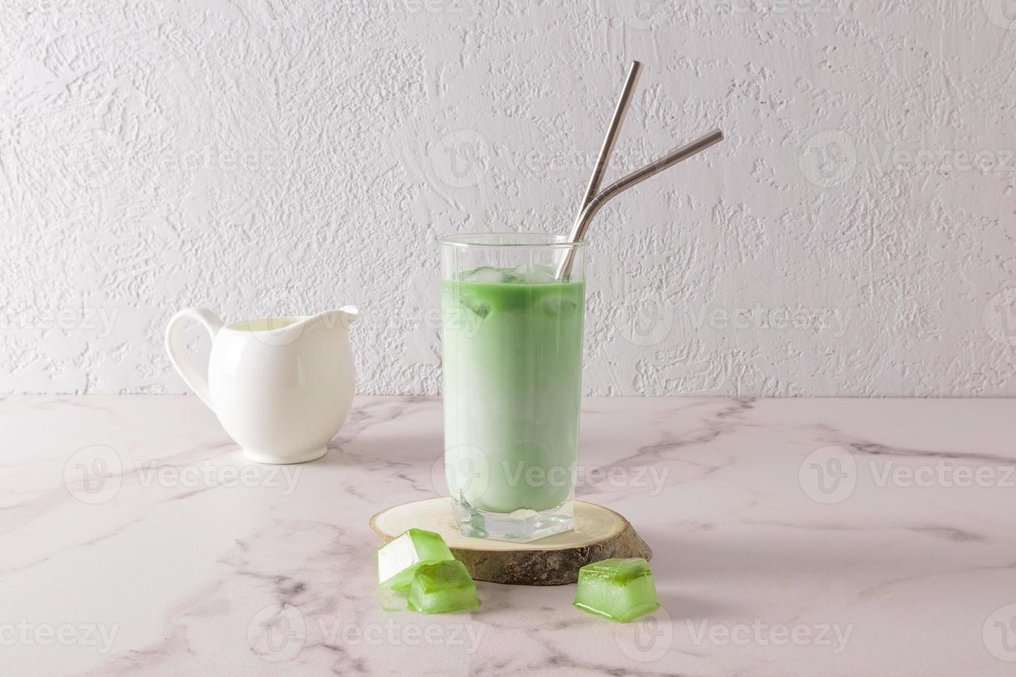 a tall glass of iced matcha tea, ice cubes stands on a wooden slice of wood on a marble white table. natural healthy drink. photo