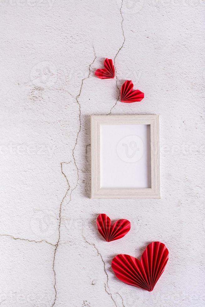 Paper red DIY hearts around an empty photo frame on a concrete. Valentine's Day. Vertical view