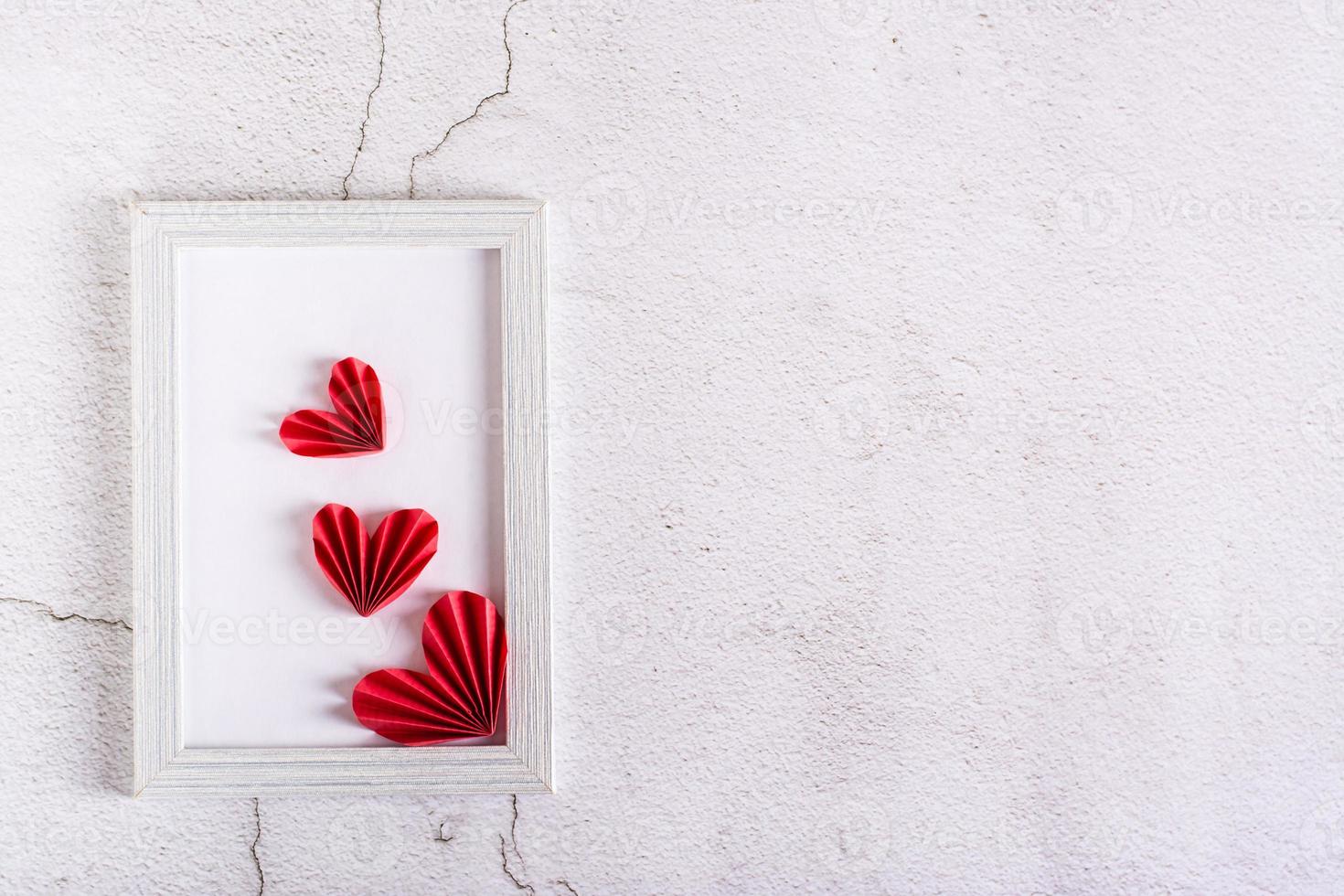 Corazones de bricolaje de papel rojo en un marco de fotos vacío sobre yeso. día de San Valentín. vista superior