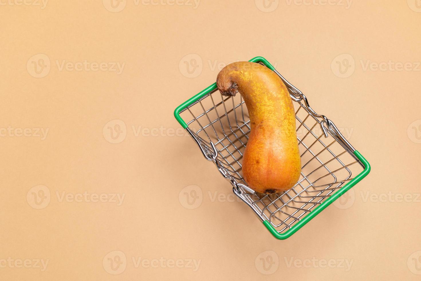 Small decorative green supermarket shopping basket with ugly curved pear on beige background. photo