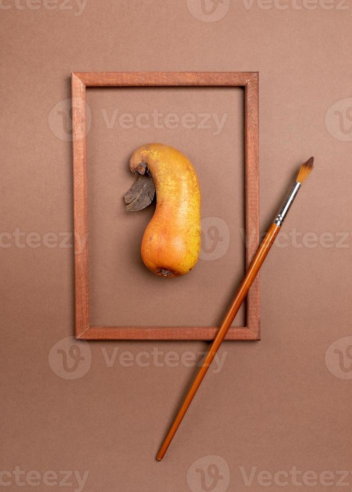 Wooden frame with ugly ripe pear inside it and brush on brown background. photo