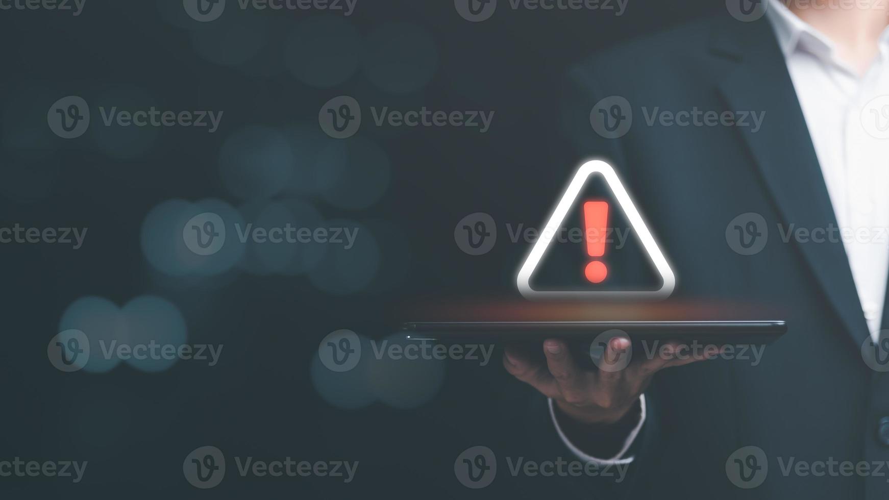 Businessman holding a tablet and showing a warning icon, exclamation mark,alarm,computer virus detected,danger warning concept or information error that should be urgently fixed and repaired photo