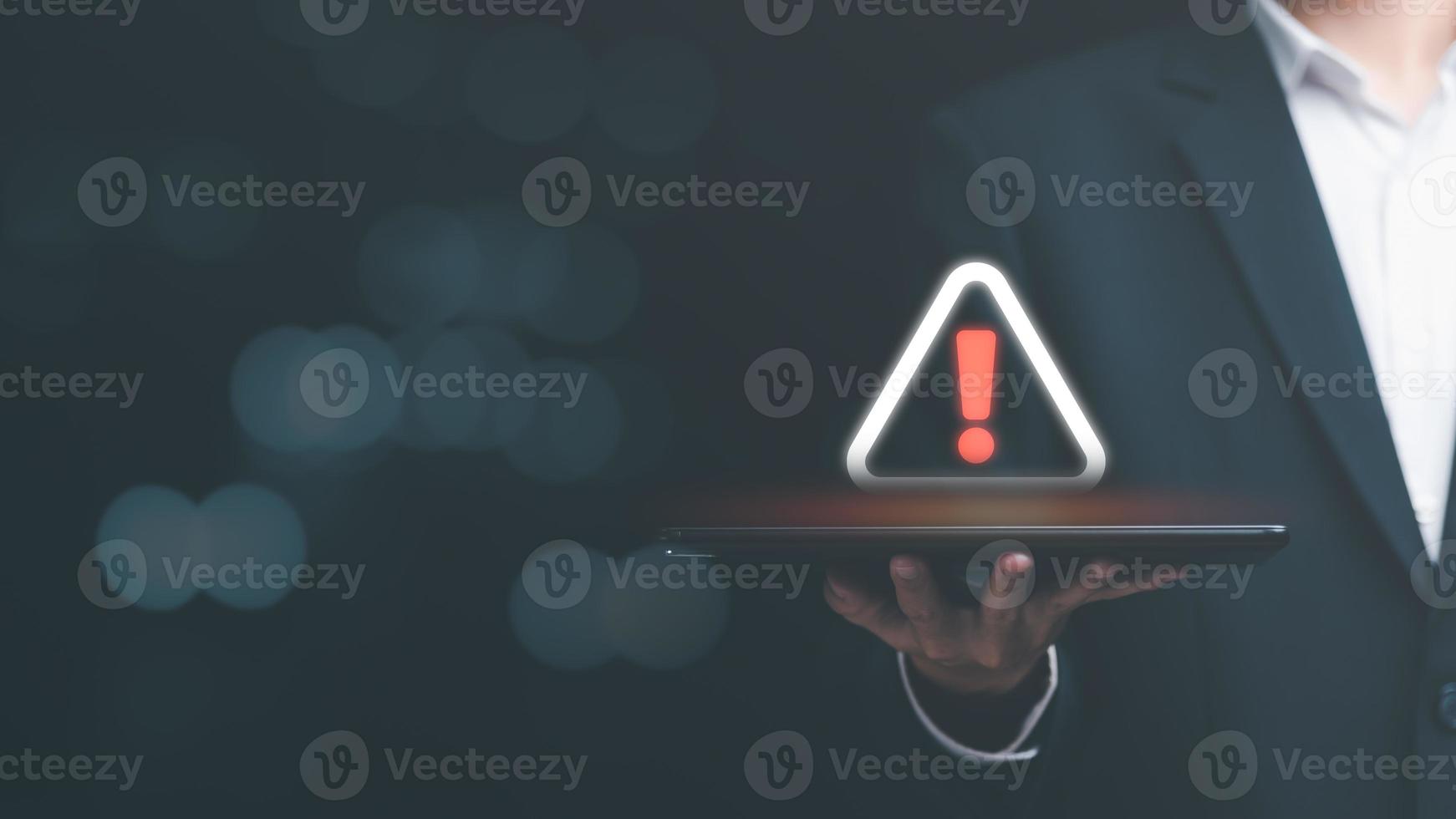 hombre de negocios que sostiene una tableta y muestra un icono de advertencia, un signo de exclamación, una alarma, un virus informático detectado, un concepto de advertencia de peligro o un error de información que debe corregirse y repararse con urgencia foto