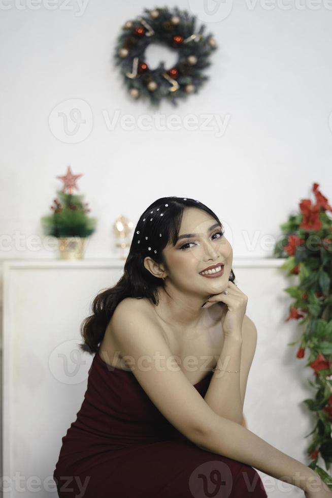 Portrait of pretty young girl cozy sit down, smiling wear red gown in decorated Christmas living room indoors photo