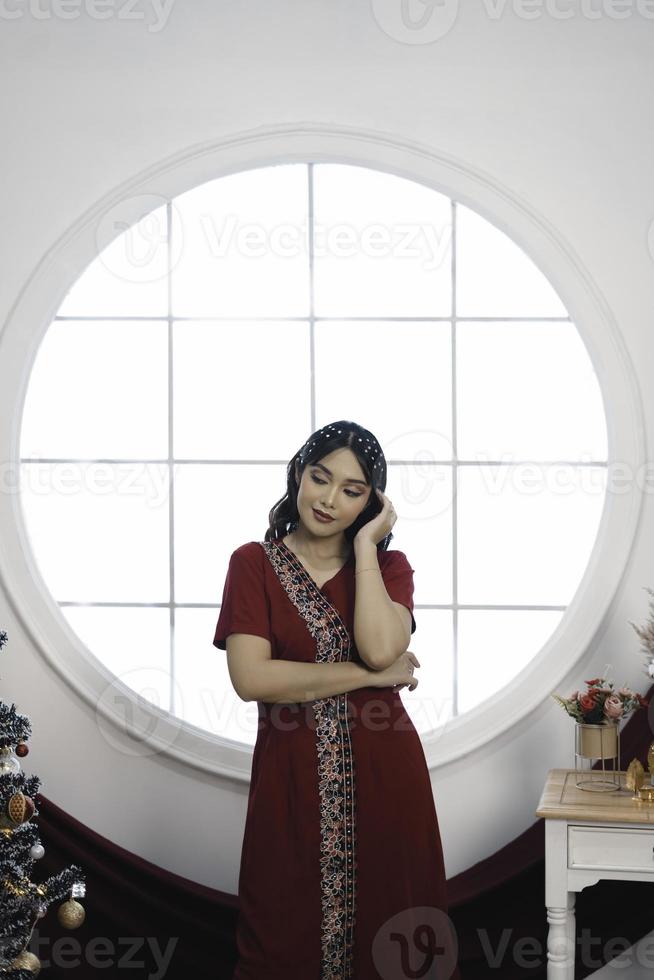 retrato de una linda joven con un vestido rojo, sonriendo a la cámara, de pie en un salón de Navidad decorado en el interior foto