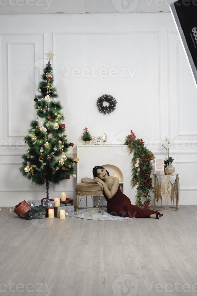 Portrait of pretty young girl cozy sit down on the floor, smiling wear red gown in decorated Christmas living room indoors photo