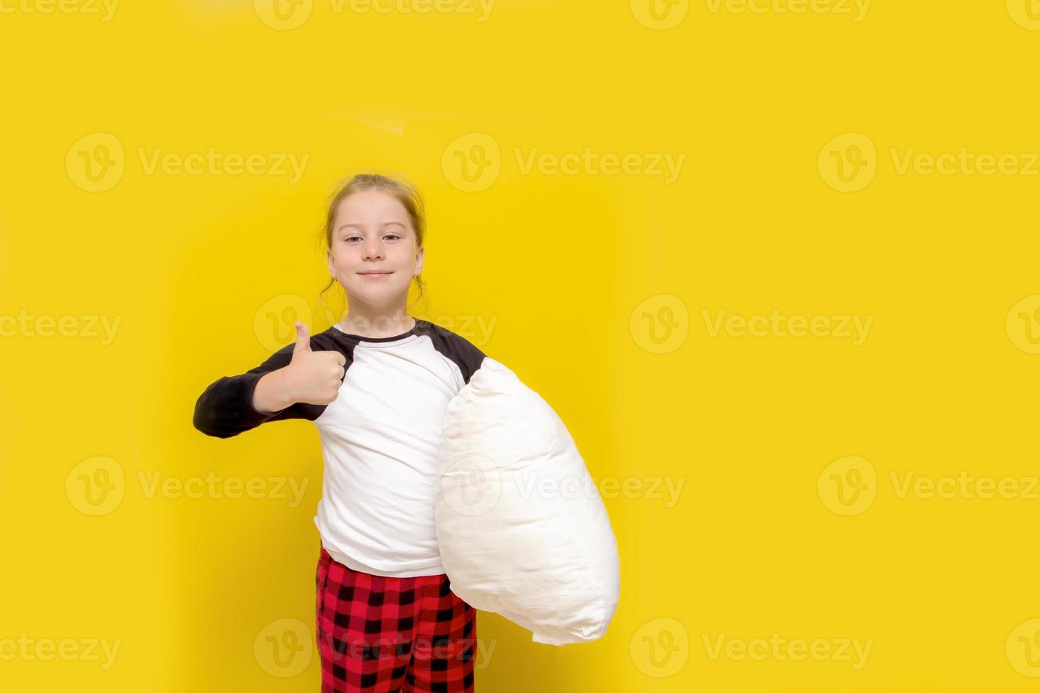 little girl in pajamas and with a pillow on a yellow background shows like photo