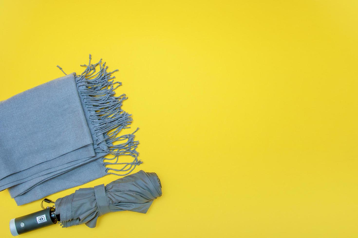 autumn accessories, gray scarf with umbrella on yellow background with copy space photo