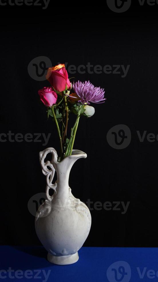 flores en un antiguo jarrón de cerámica blanca sobre fondo oscuro en formato vertical foto