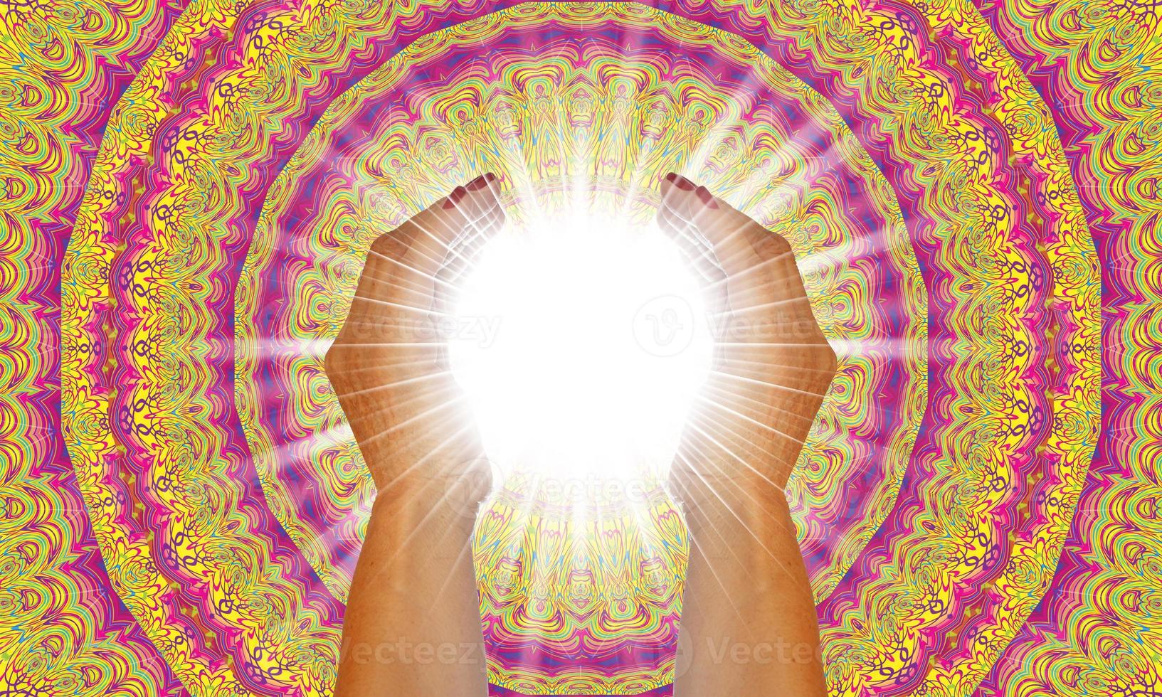Rays of white light between the hands of a woman with multicolored mandala background photo