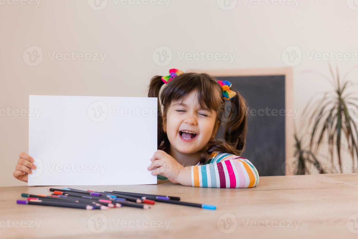 a cute little girl in a drawing lesson holds an empty white sheet in her hands, a space for text. Children and creativity. High quality photo