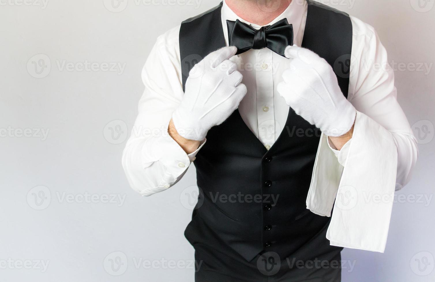 retrato de camarero o mayordomo con guantes blancos alisando la corbata de moño sobre fondo blanco. concepto de industria de servicios y cortesía profesional. foto