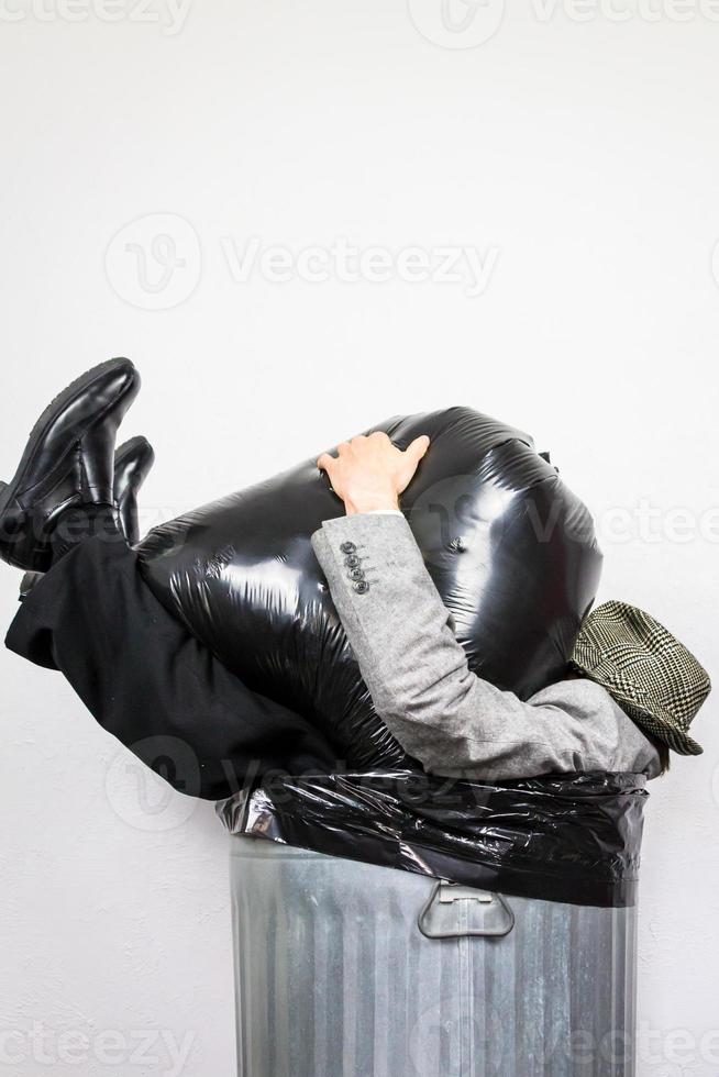 Businessman Sitting in Trash Can Being Crushed by Garbage Bag. Concept of Over a Barrel. Beaten and Drowning in Waste. photo