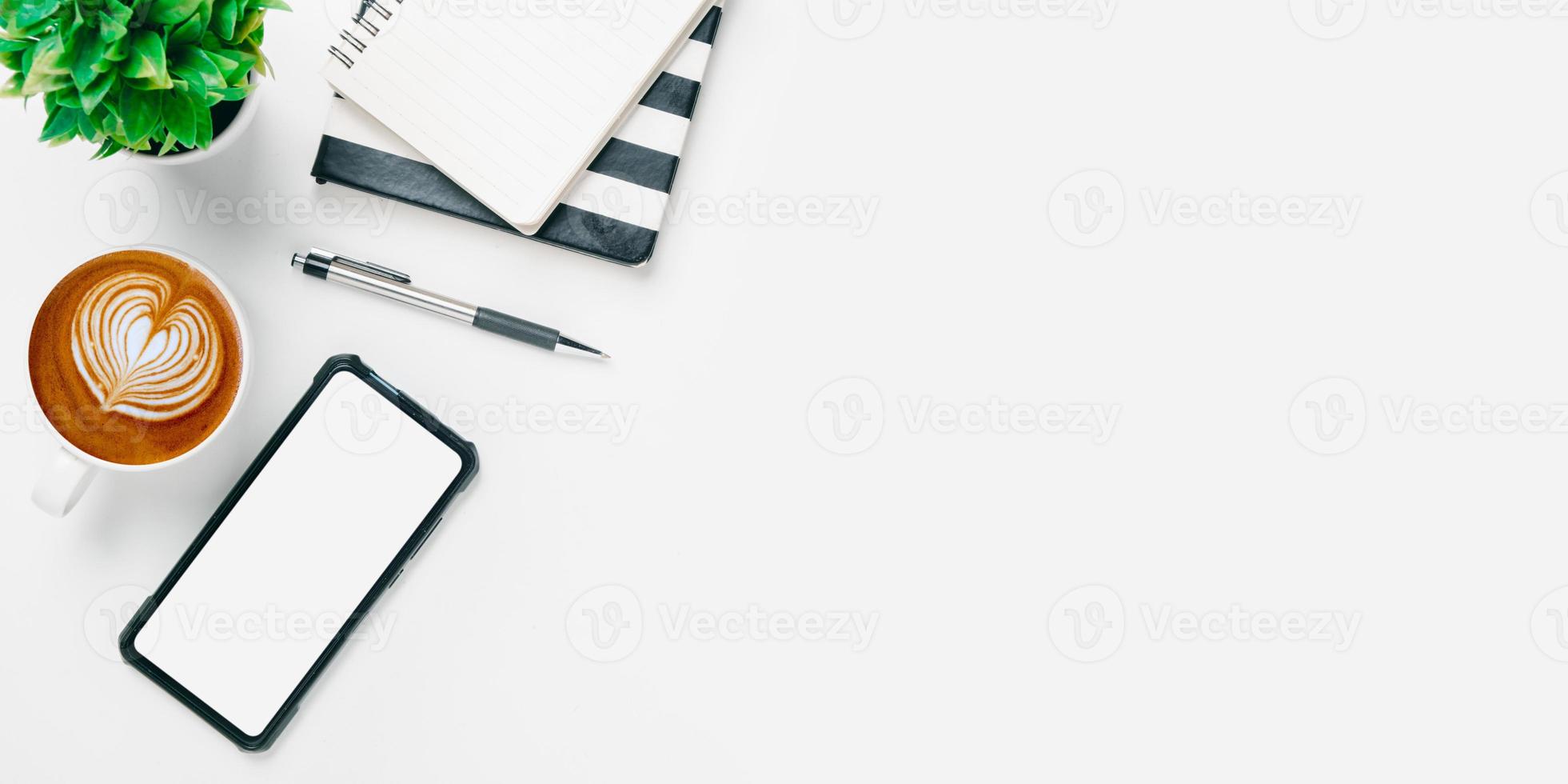 escritorio de oficina con teléfono inteligente de pantalla en blanco, bolígrafo, cuaderno, taza de café sobre fondo blanco, vista superior con espacio de copia, maqueta. foto